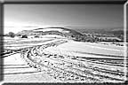 Tracks in a snow covered field leading toward distant hills.