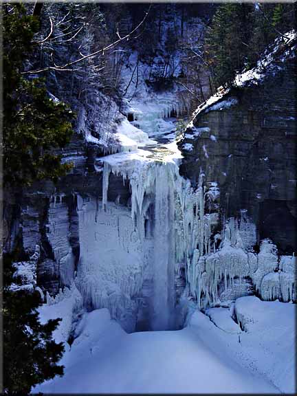 The winter sun streams over the top of a frozen taughannock Falls.