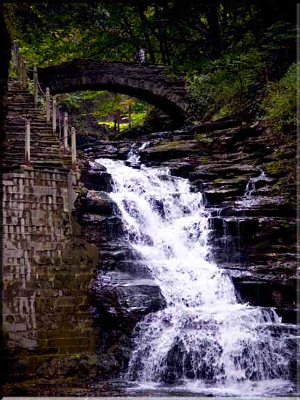 Looking up at the waterfall rushing out below the stone bridge.
